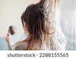 Close up of woman touching dirty oily and greasy hair looking in mirror at home. Time to wash head with high-quality shampoo. Back view