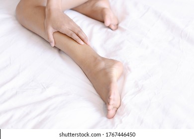 Close Up Woman Touching Her Leg With Pain Lying On White Bed, Health Care Concept