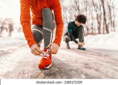 Close Up Of Woman Tying Shoelace While Crouching On The Trail At Winter. Outdoor Fitness Concept. In Background Man..