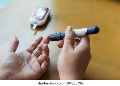 Close up of woman use lancet on finger to checking blood sugar level by Glucose meter using as Medicine, diabetes, glycemia, health care and people concept.