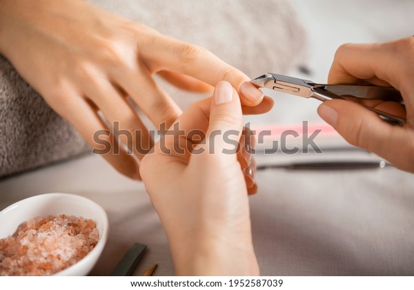 Close up of a woman using a cuticle clipper to\
give a nail manicure. Woman remove a cuticle nail with steel nail\
clipper. Manicurist using a stainless pusher for cuticle on hands\
during treatment.