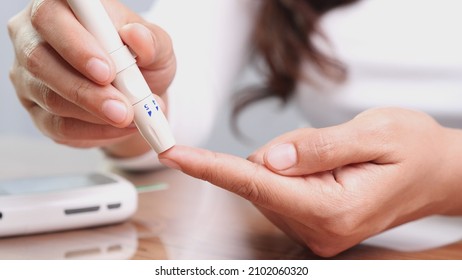 Close up of woman using lancet pen on finger with blood drop testing concentration of glucose in blood by Glucose meter. Concept of World Diabetes Day, Glycemia, Hypoglycemia, Hyperglycemia, Insulin