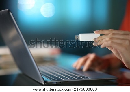 Close up of a woman using a laptop with her hand holding a pen drive in the night at home