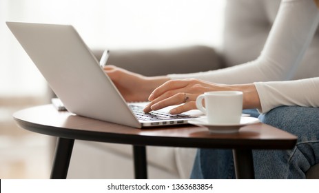 Close up woman using laptop, sitting on sofa, female hands typing, writing notes, studying languages, distance learning concept, checking email in morning, drink coffee, working at home