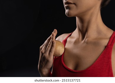 Close up of woman using wooden massage ball on chest wearing red tank top on dark background, self care and relaxation techniques. self massage tool - Powered by Shutterstock