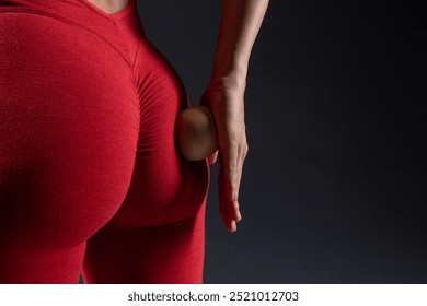 Close up of woman using wooden yoga massage ball on buttock in red tank top on dark background, self care and relaxation techniques. Self massage tool, cellulite removal concept - Powered by Shutterstock