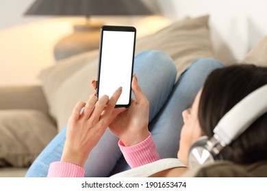 Close up of a woman wearing headphones checking blank screen on mobile phone lying on a couch at home