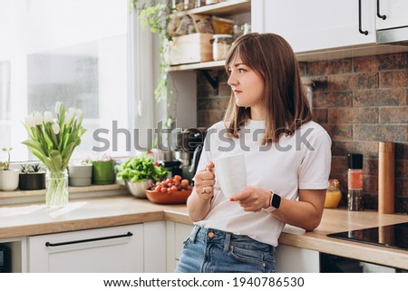 Close up woman in white t-shirt drinking coffee or tea in kitchen at home. Early breakfast in the morning, rest time
