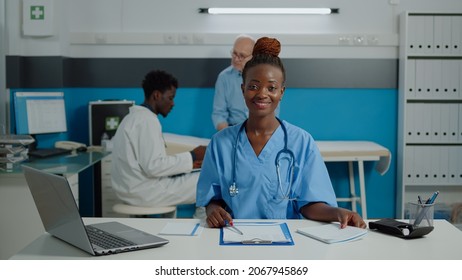 Close Up Of Woman Working As Nurse Sitting At Desk And Reading Documents, Files, Papers Of Patient Checkup. Person Wearing Uniform And Stethoscope In Healthcare Cabinet At Facility