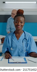 Close Up Of Woman Working As Nurse Sitting At Desk And Reading Documents, Files, Papers Of Patient Checkup. Person Wearing Uniform And Stethoscope In Healthcare Cabinet At Facility