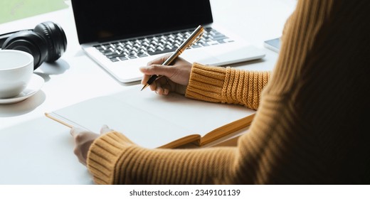Close up of woman writing taking notes while sitting in front her computer laptop at the working table living room - Shutterstock ID 2349101139