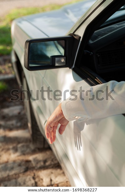 Close up of a womans arm and hand hanging out of a\
white car