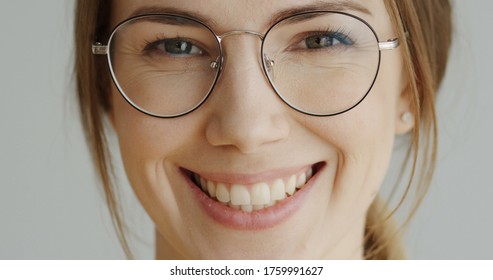 Close Up Of The Woman's Face In Glasses With Fair Hair Looking Straight In The Camera And Smiling On The White Wall Background. Portrait. Inside