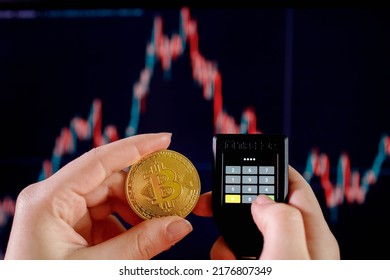 Close up womans hand holding bitcoin and enter the password on cryptocurrencey hardware cold wallet on stock market graph background. Secure cryptocurrency storage.
