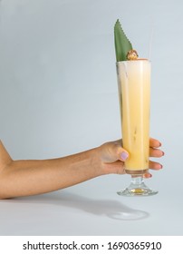 Close Up Of A Woman's Hand Holding A Glass Of Tropical Pina Colada Cocktail On White Background With Copy Space. Summer Time Vacation Concept.