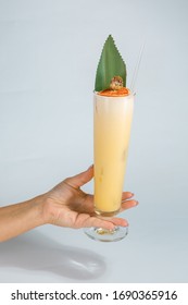 Close Up Of A Woman's Hand Holding A Glass Of Tropical Pina Colada Cocktail On White Background With Copy Space. Summer Time Vacation Concept.