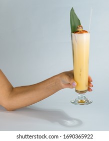 Close Up Of A Woman's Hand Holding A Glass Of Tropical Pina Colada Cocktail On White Background With Copy Space. Summer Time Vacation Concept.