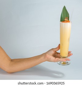 Close Up Of A Woman's Hand Holding A Glass Of Tropical Pina Colada Cocktail On White Background With Copy Space. Summer Time Vacation Concept.