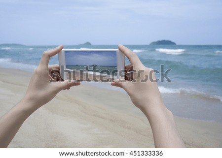 Close up of woman's hand holding smart phone, mobile, smart phone over blurred beautiful blue sea to take a photo of the sea