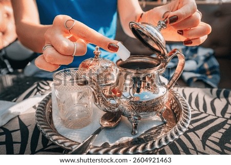 Close up of woman's hands adding sugar cube to a silver teapot, preparing traditional Moroccan mint tea