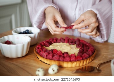 Close up of woman's hands decorating raspberry tart, cooks delicious pie with fresh berries and cream cheese - Powered by Shutterstock