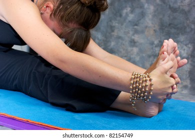 Close up of a woman's hands and feet as she bends over in a yogic forward fold or Paschimottasana on yoga mat in studio wearing mala beads.