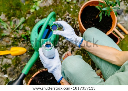 Close up of woman's hands in gloves pours liquid mineral fertilizer in watering can with water in backyard. Cultivation and caring for outdoor potted plants. Hobbies and leisure, urban jungle concept. Stock photo © 