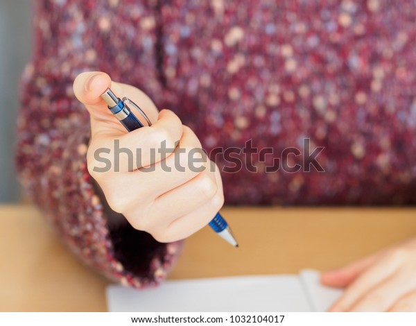 Close up of woman\'s hands hold a Mechanical\
pencil with notepad placed on wooden\
table.