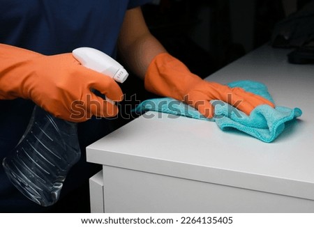 close up of woman's hands in orange rubber gloves cleaning white dresser surface 