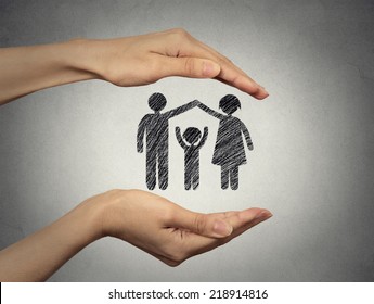 Close Up Of Woman's Hands Protecting Happy Family, Mother, Father, Child. Family Abstract In Palms On Grey Wall Background. Safe Childhood, Parenting. Love Care Compassion Safety Secure Future Concept