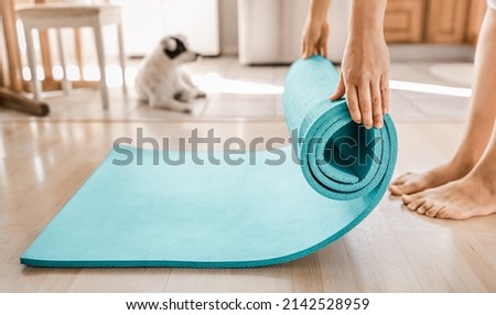 Close up of a woman's hands is rolling up exercise mat and preparing to doing yoga. Exercising on floor mat  at home.