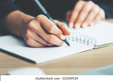 Close up of woman's hands writing in spiral notepad placed on wooden desktop with various items - Shutterstock ID 525439534