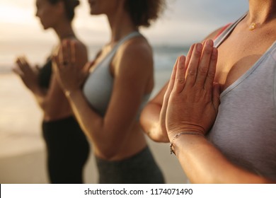 Close up of women doing yoga standing at the beach with joined palms and closed eyes. Three women in fitness wear doing yoga and meditation standing at the seashore. - Shutterstock ID 1174071490