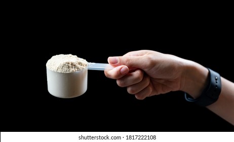 Close up of women hand holding measuring scoop of whey protein  preparing protein shake.