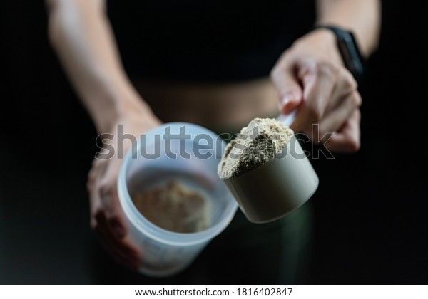 Close up of women with measuring\
scoop of whey protein and shaker bottle, preparing protein\
shake.