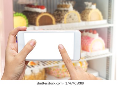 Close up women's hands hold and touch screen smartphone or cellphone with blank white screen for put it on your own webpage or message over blurred cake in refrigerator background