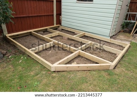 close up of wooden decking base being built in a garden against a lawn and shed.  The garden is a domestic piece of ground outside a home in autumn