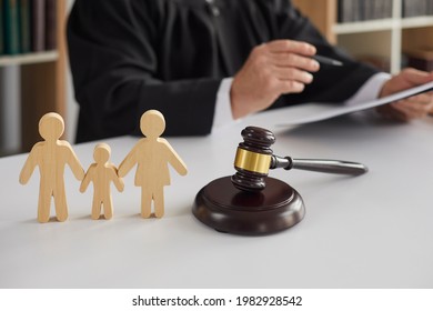 Close Up Of Wooden Figurines Of Family With Child And Gavel On Background Of Judge Conducting Divorce Process. Concept Of Alimony, Family Law And Child Custody.