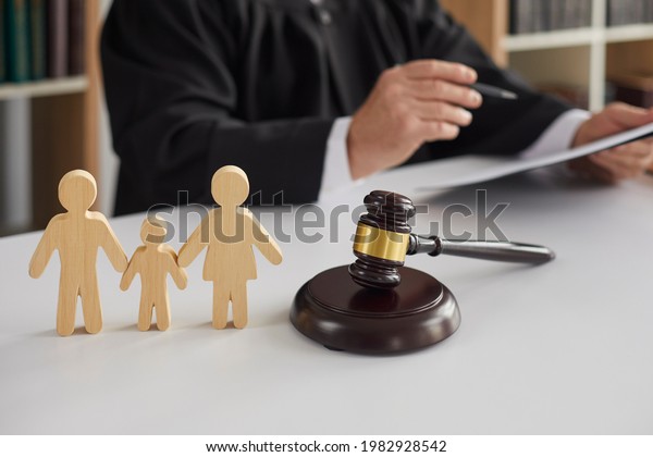 Close up of wooden figurines of family\
with child and gavel on background of judge conducting divorce\
process. Concept of alimony, family law and child\
custody.