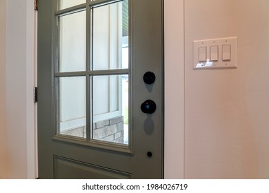 Close Up Of Wooden Front Door Of Home With Glass Panel And Black Doorknob. White Wooden Wall And Brick Wall Can Be Seen On The Other Side Of The Door.