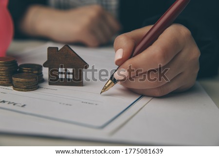 Close up wooden toy house with Woman signs a purchase contract or mortgage for a home, Real estate concept.