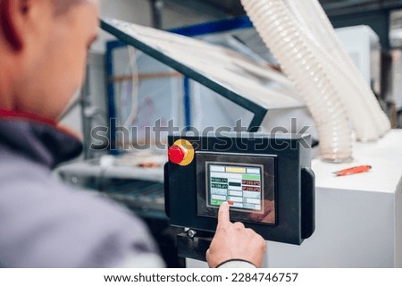 Close up of a woodworker's hand pressing commands on a dashboard on a machine. Selective focus on hand adjusting settings on a wood processing machine at the carpentry workshop.