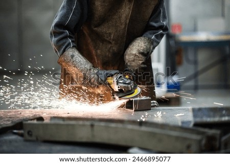 Close up of work of welder in workshop, operating welding machine, wearing protective clothing and a welding mask.