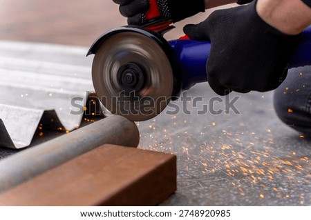 Close up of worker cutting metal pipe with angle grinder, producing sparks on concrete ground outdoors.
