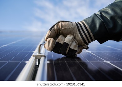 Close up of worker hand in glove holding a hex key, installing photovoltaic solar panel with blue sky on background. Electrician mounting solar photovoltaic panel system. Concept of alternative energy