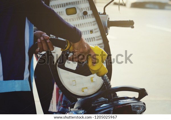 close up worker hand\
holding nozzle fuel fill oil into motorcycle tank at pump gas\
station, transport energy, transportation power business technology\
concept, vintage tone