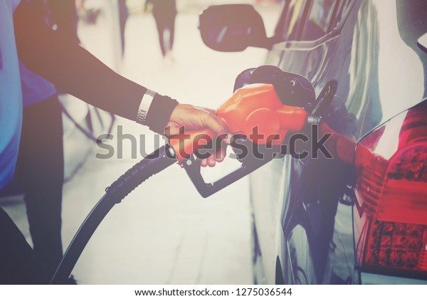 close up worker hand holding\
nozzle fuel fill oil into car tank at pump gas station, vintage\
tone