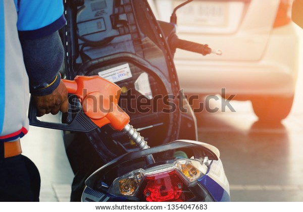 close up worker hand holding nozzle\
fuel fill oil into motorcycle tank at pump gas station, transport\
energy, transportation power business technology\
concept