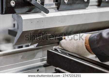 Close up of worker hands in gloves using hydraulic press brake for precision metal sheet bending.
