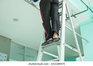 Close Up Of Worker Legs Standing On Ladder In Home Improvement. Risk Management Concept.